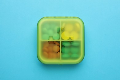 Pill box with medicaments on light blue background, top view