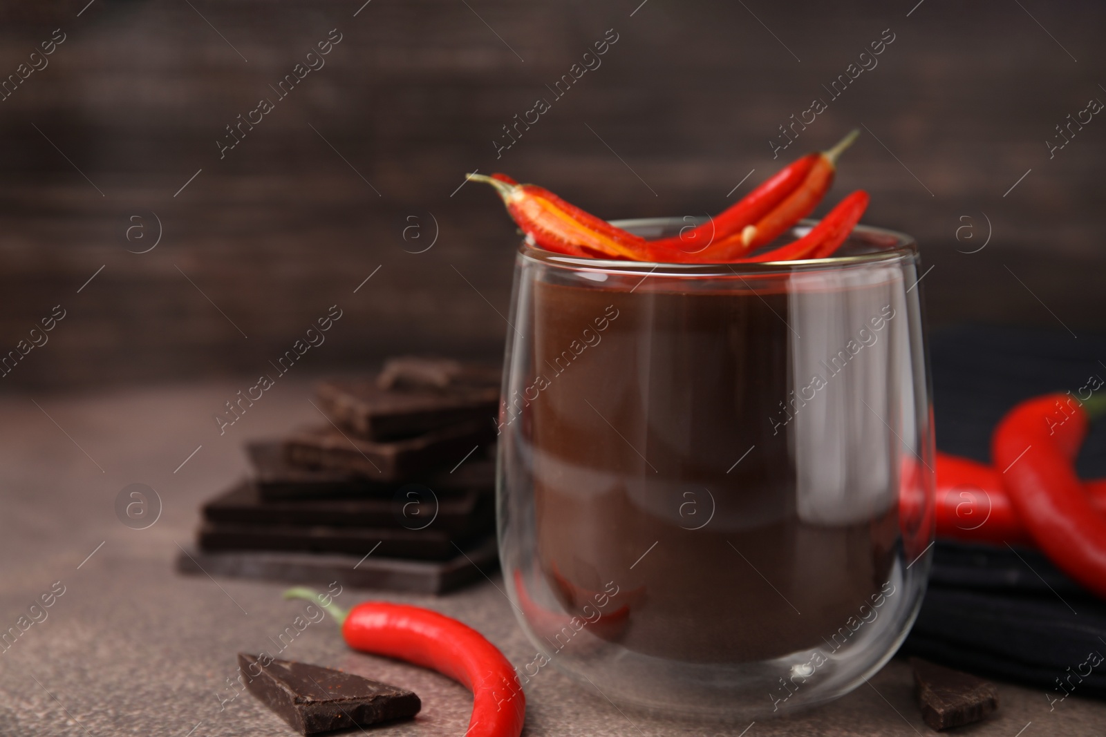 Photo of Delicious hot chocolate with chili peppers on brown textured table, closeup. Space for text