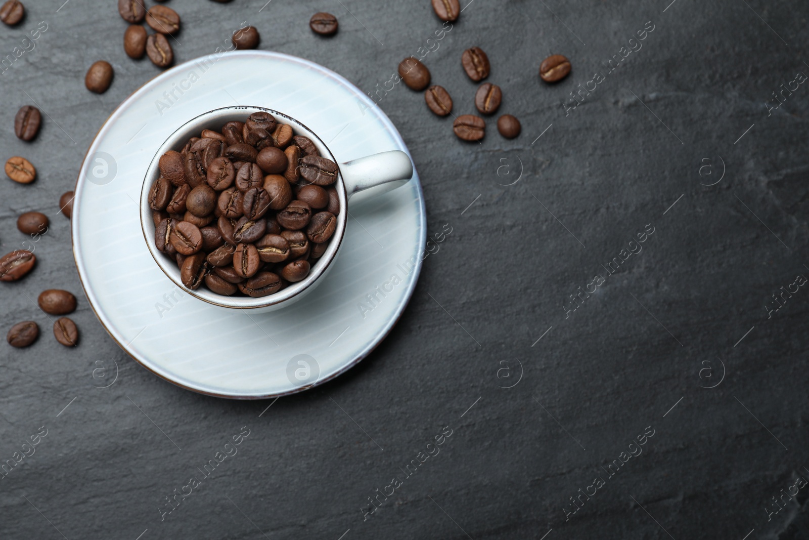 Photo of Cup with roasted coffee beans on black table, flat lay. Space for text