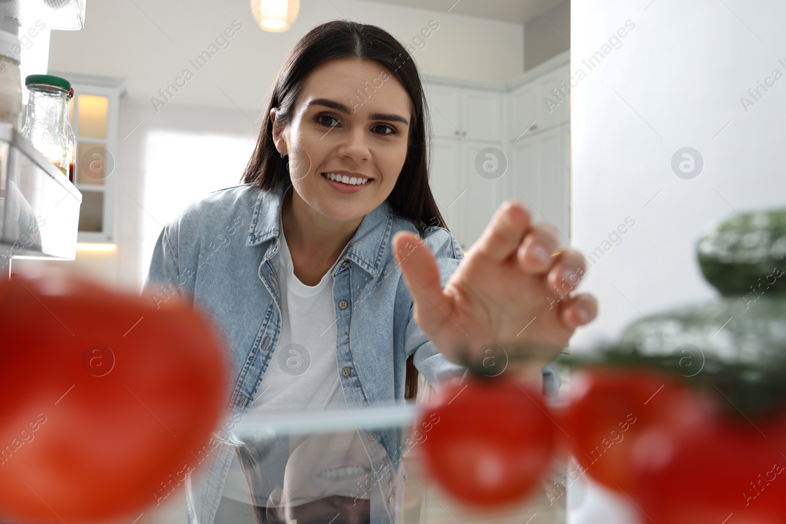 Photo of Young woman near refrigerator in kitchen, view from inside