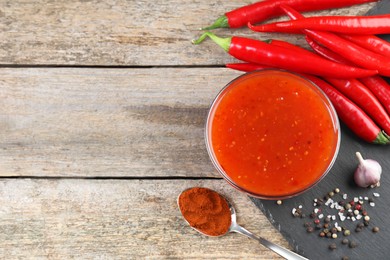 Photo of Spicy chili sauce in bowl and ingredients on wooden table, flat lay. Space for text