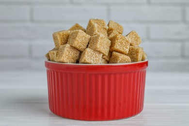 Photo of Brown sugar cubes in bowl on white wooden table, closeup