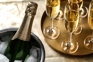 Bottle of champagne in bucket with ice and glasses on table, closeup. Space for text