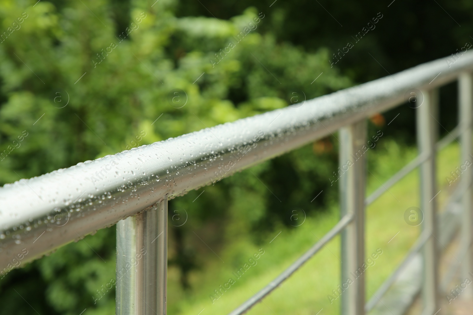 Photo of Metal handrail with water drops outdoors, closeup. Rainy weather