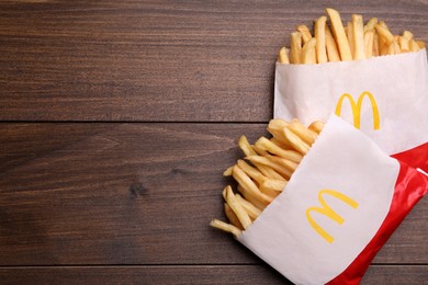 Photo of MYKOLAIV, UKRAINE - AUGUST 12, 2021: Two small portions of McDonald's French fries on wooden table, flat lay. Space for text