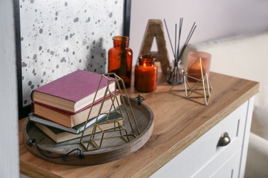Photo of Wooden tray with books and decor on chest of drawers indoors