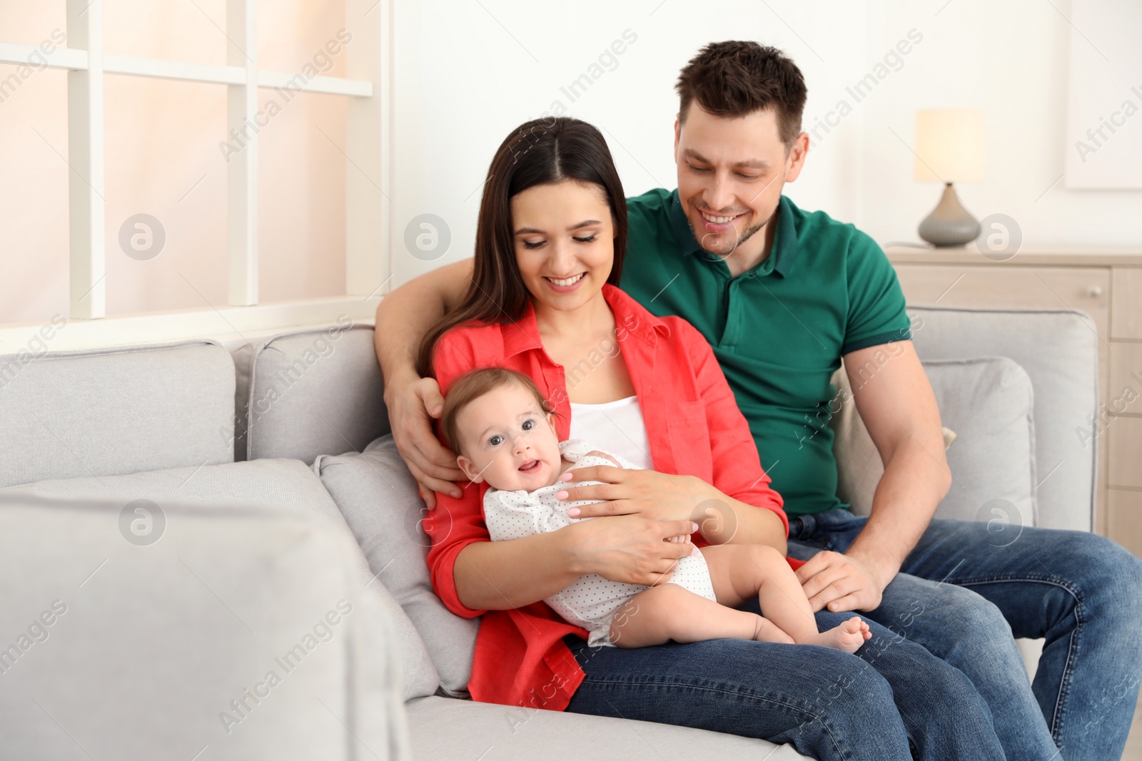 Photo of Happy couple with adorable baby on sofa at home. Family time