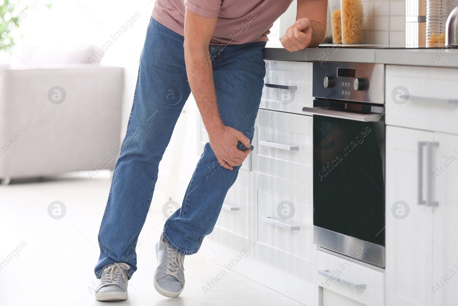 Photo of Senior man suffering from knee pain in kitchen, closeup