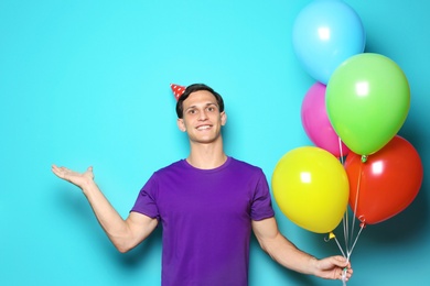 Young man with bright balloons on color background. Birthday celebration