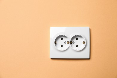 Double power socket on pale orange wall, space for text. Electrical supply