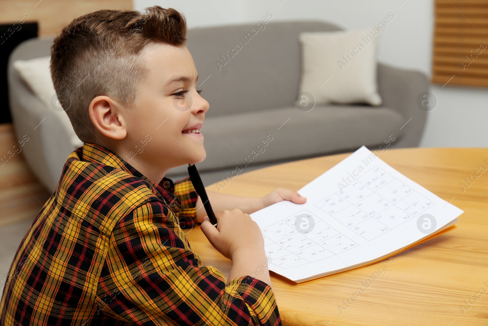 Photo of Little boy solving sudoku puzzle at table indoors