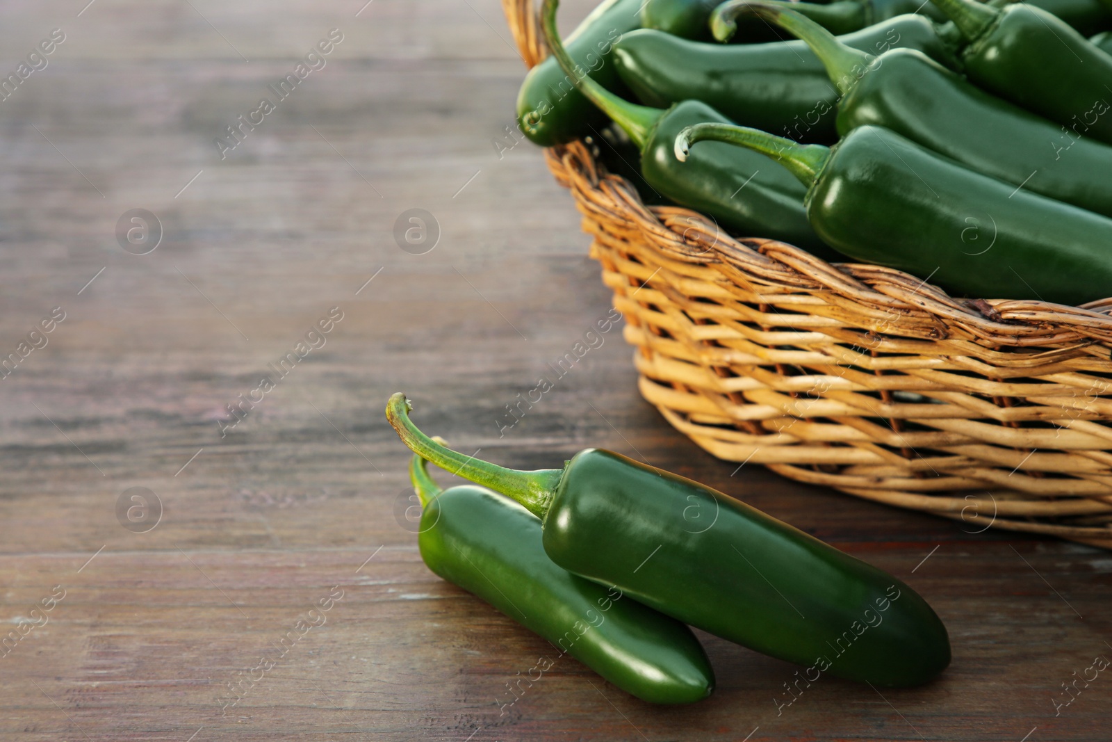 Photo of Wicker basket with green jalapeno peppers on wooden table, closeup. Space for text