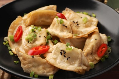 Photo of Delicious gyoza (asian dumplings) with sesame seeds, green onions and chili peppers in bowl, closeup