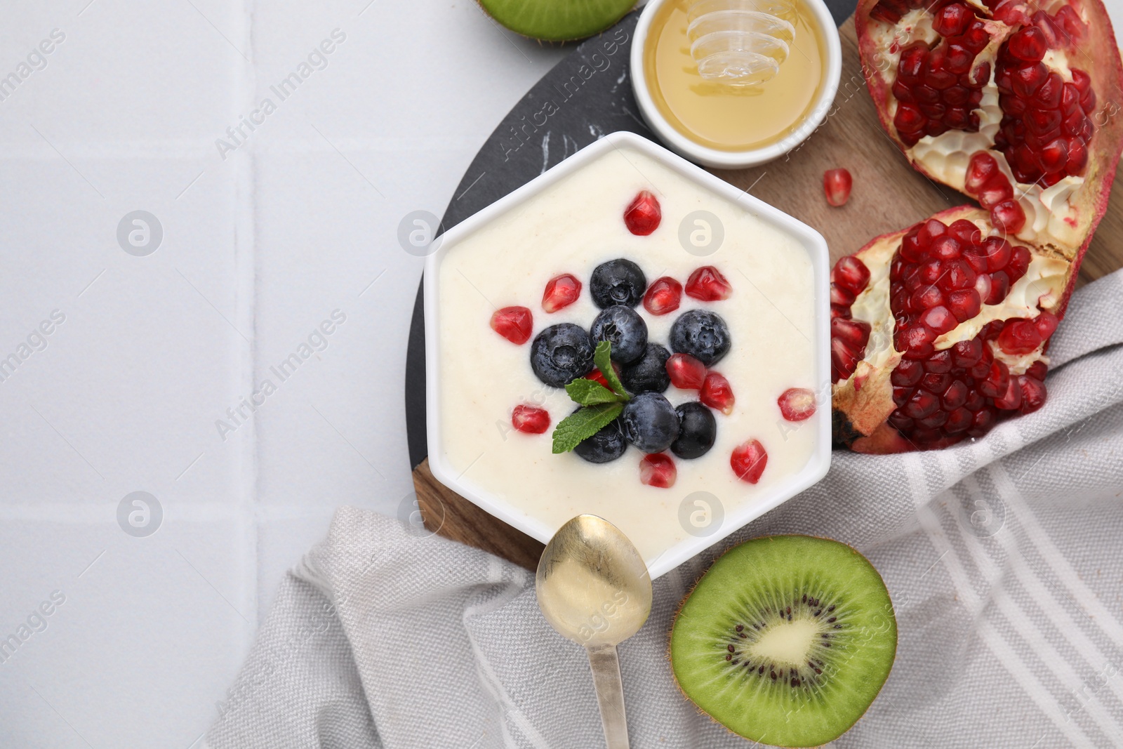 Photo of Bowl of delicious semolina pudding with blueberries, pomegranate and mint served on white table, flat lay. Space for text