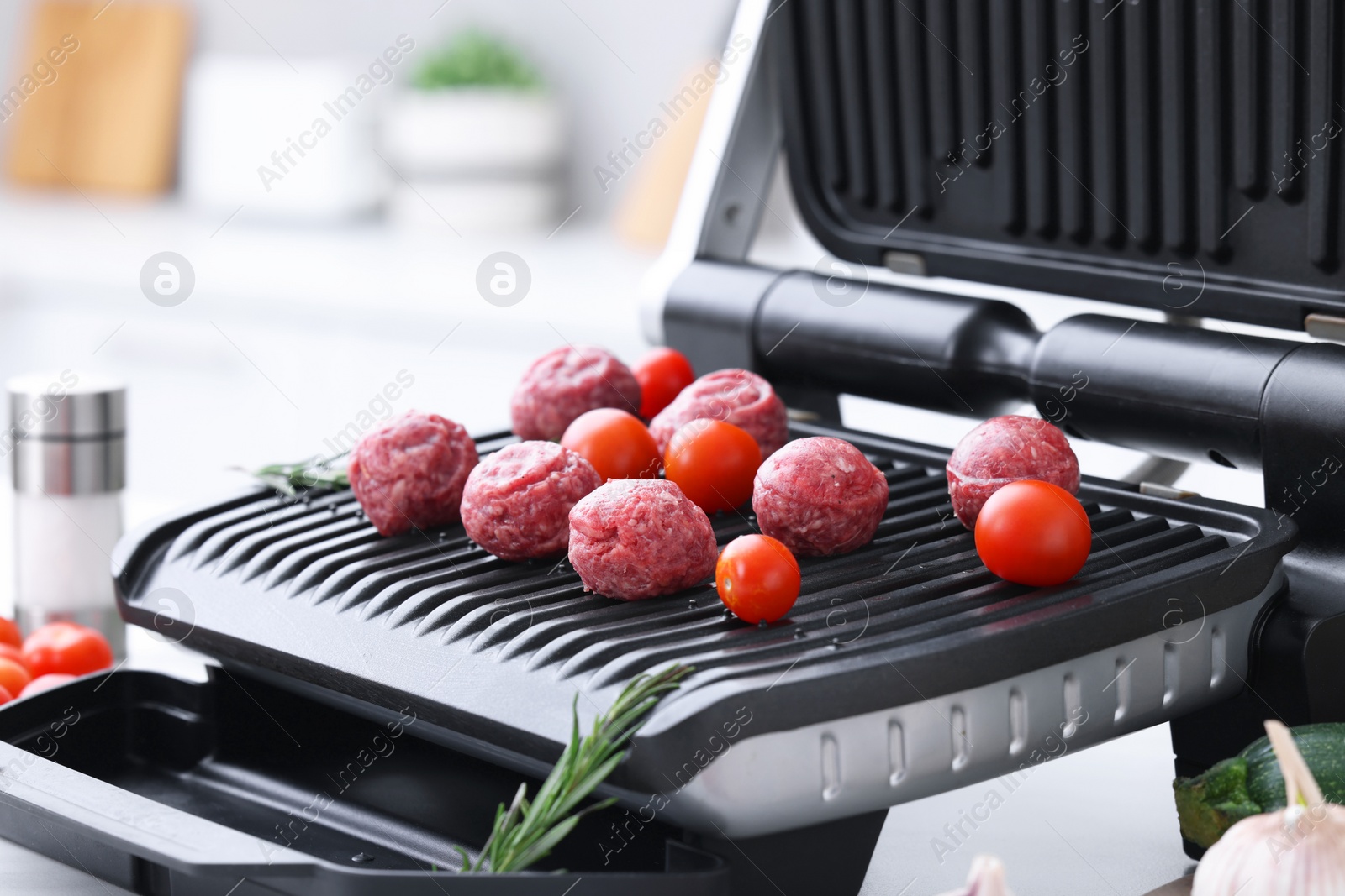 Photo of Meatballs, tomatoes and rosemary on electric grill indoors, closeup