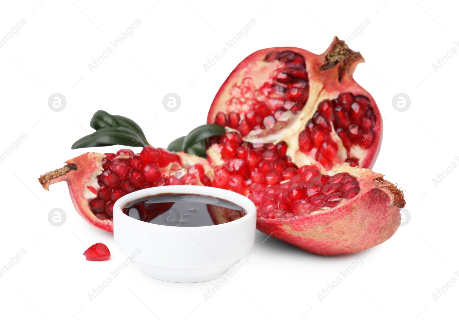 Photo of Tasty pomegranate sauce in bowl, leaves and fruits isolated on white