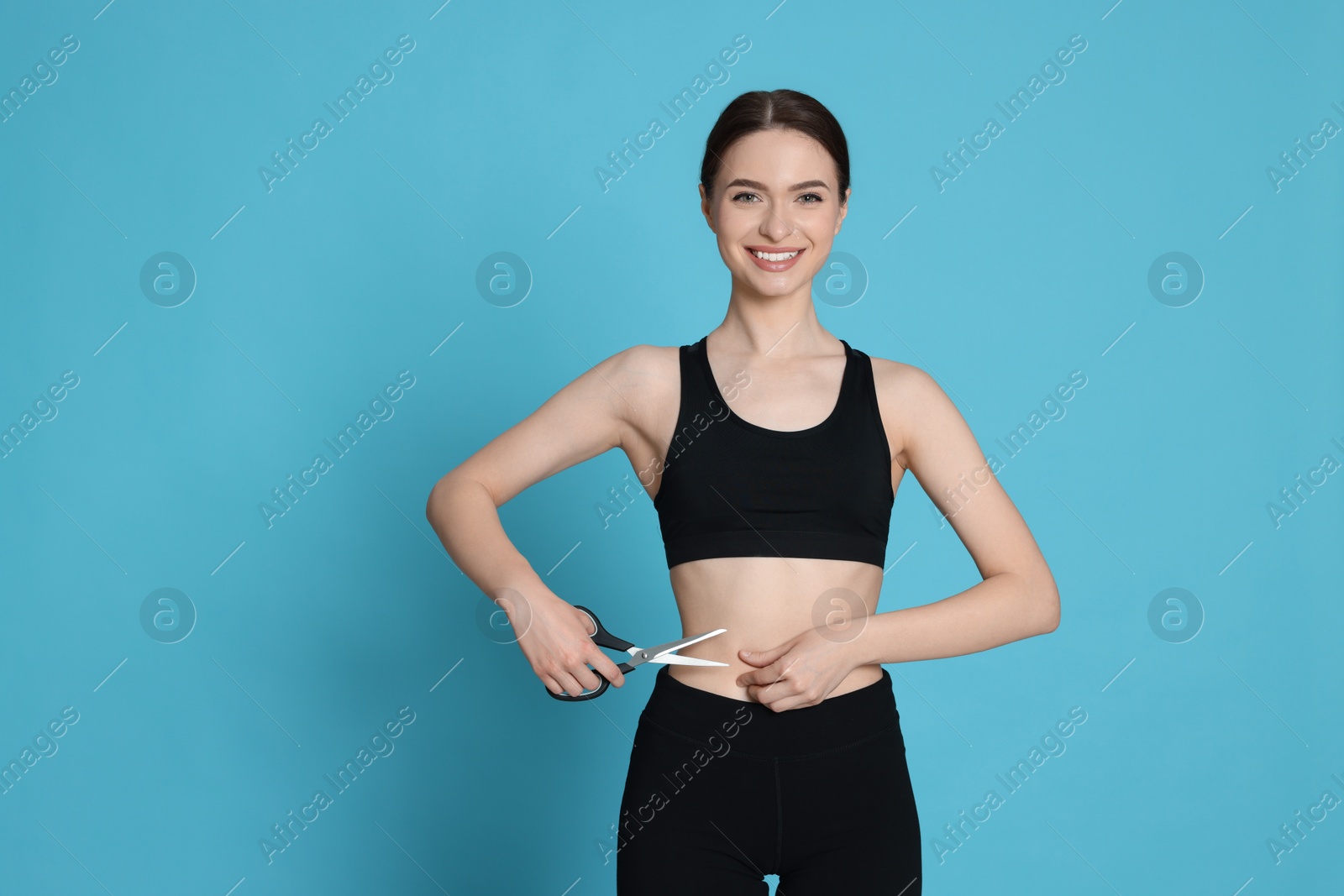 Photo of Slim young woman with scissors on light blue background, space for text. Weight loss surgery