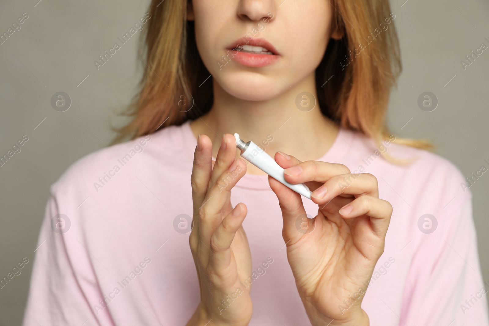 Photo of Woman with herpes applying cream onto finger against light grey background, closeup