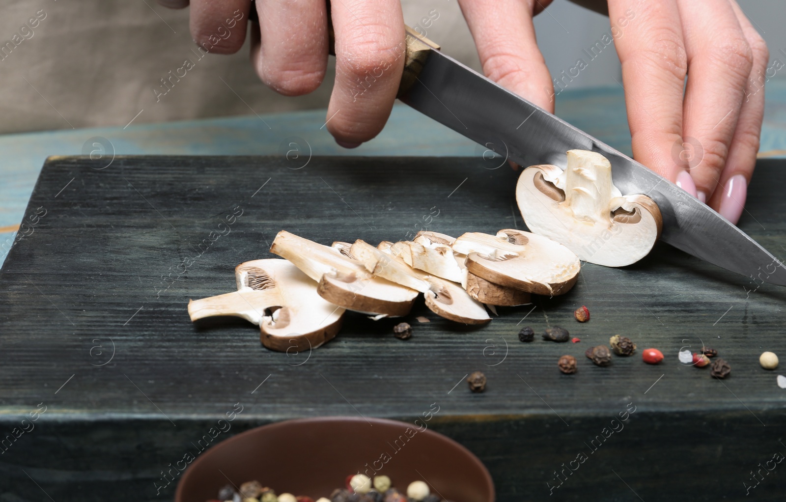 Photo of Young woman cutting fresh champignon mushrooms on wooden board, closeup view