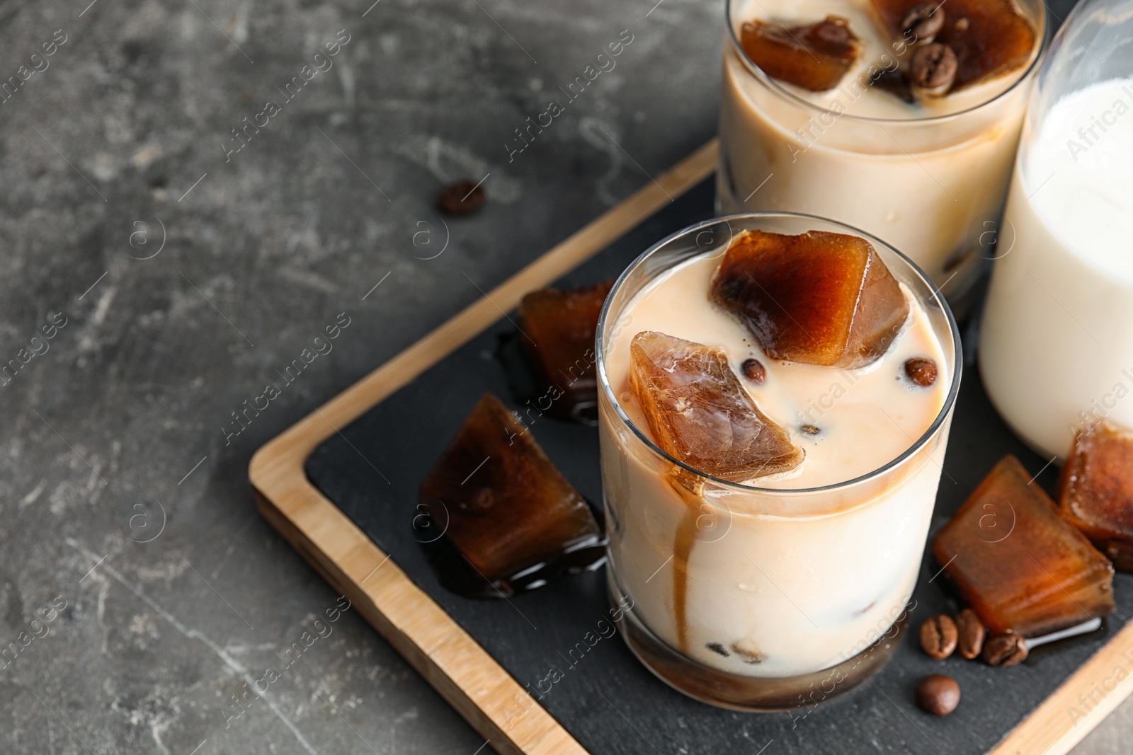 Photo of Glasses of milk with coffee ice cubes on grey table. Space for text