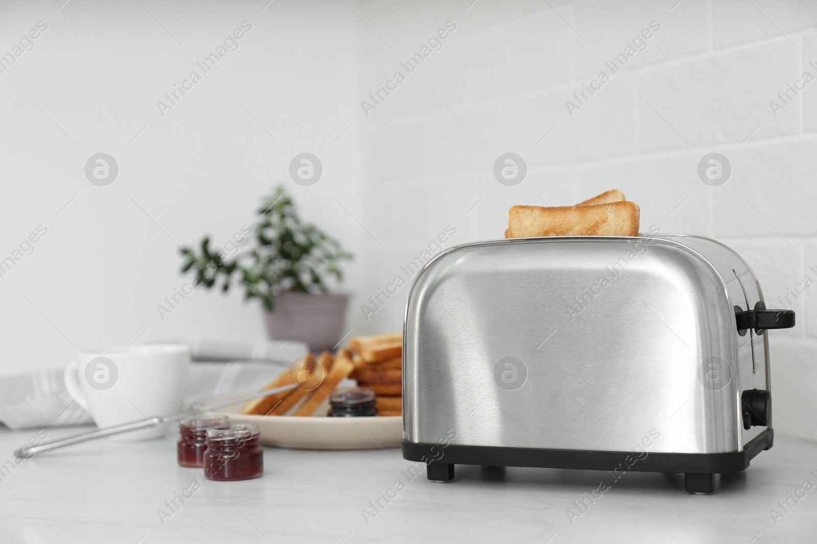 Photo of Modern toaster with slices of bread and different jams  on white table in kitchen