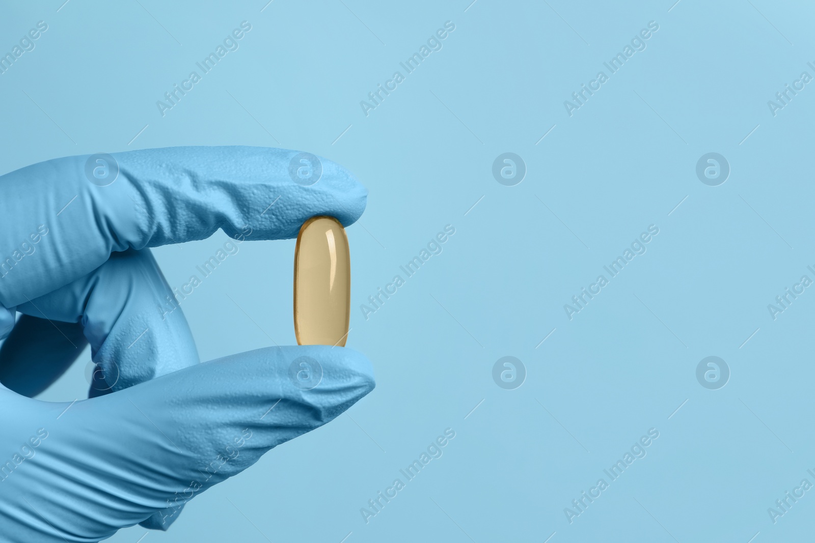 Photo of Doctor holding pill on light blue background, closeup. Space for text