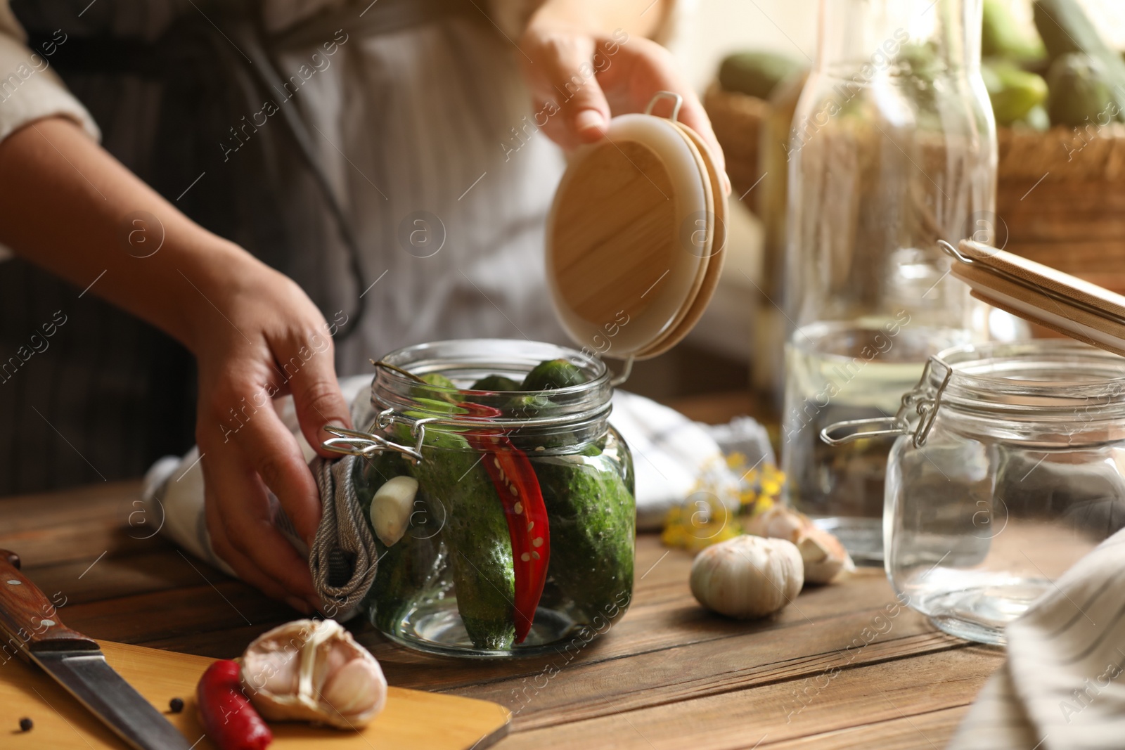 Photo of Woman pickling glass jar of cucumbers at wooden table, closeup