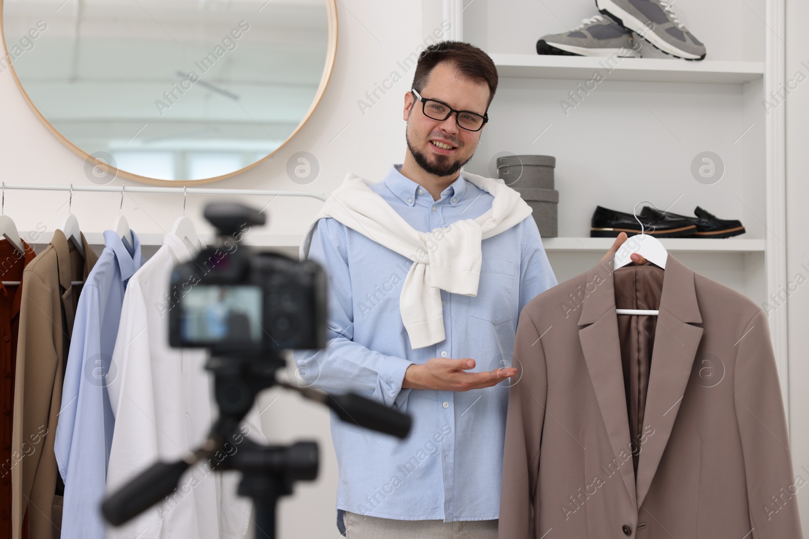 Photo of Smiling fashion blogger showing clothes while recording video at home