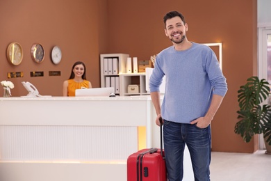 Photo of Young man with luggage near reception desk in hotel