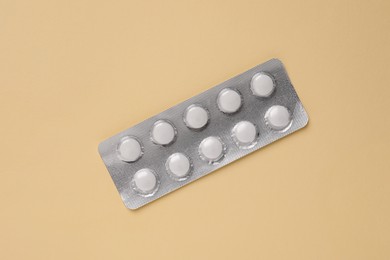 White pills in blister on beige background, top view