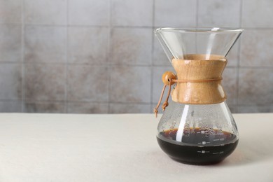 Photo of Glass chemex coffeemaker with tasty drip coffee on white table. Space for text