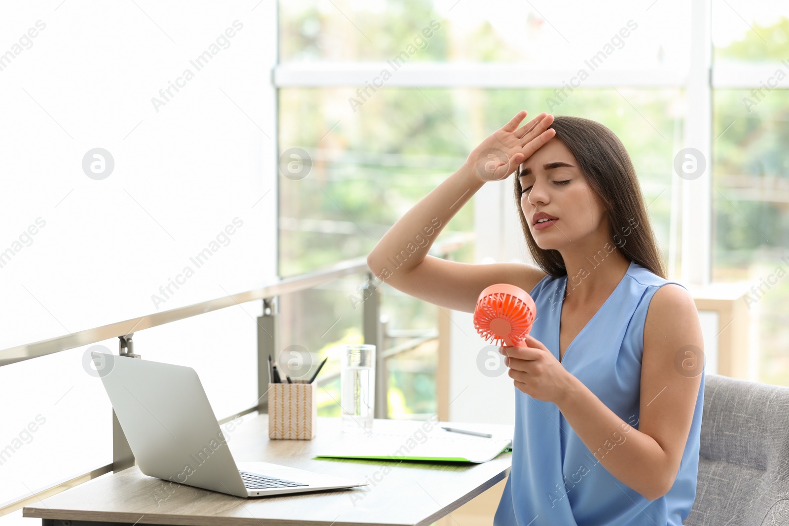 Photo of Young woman with portable fan suffering from heat at workplace, space for text. Summer season