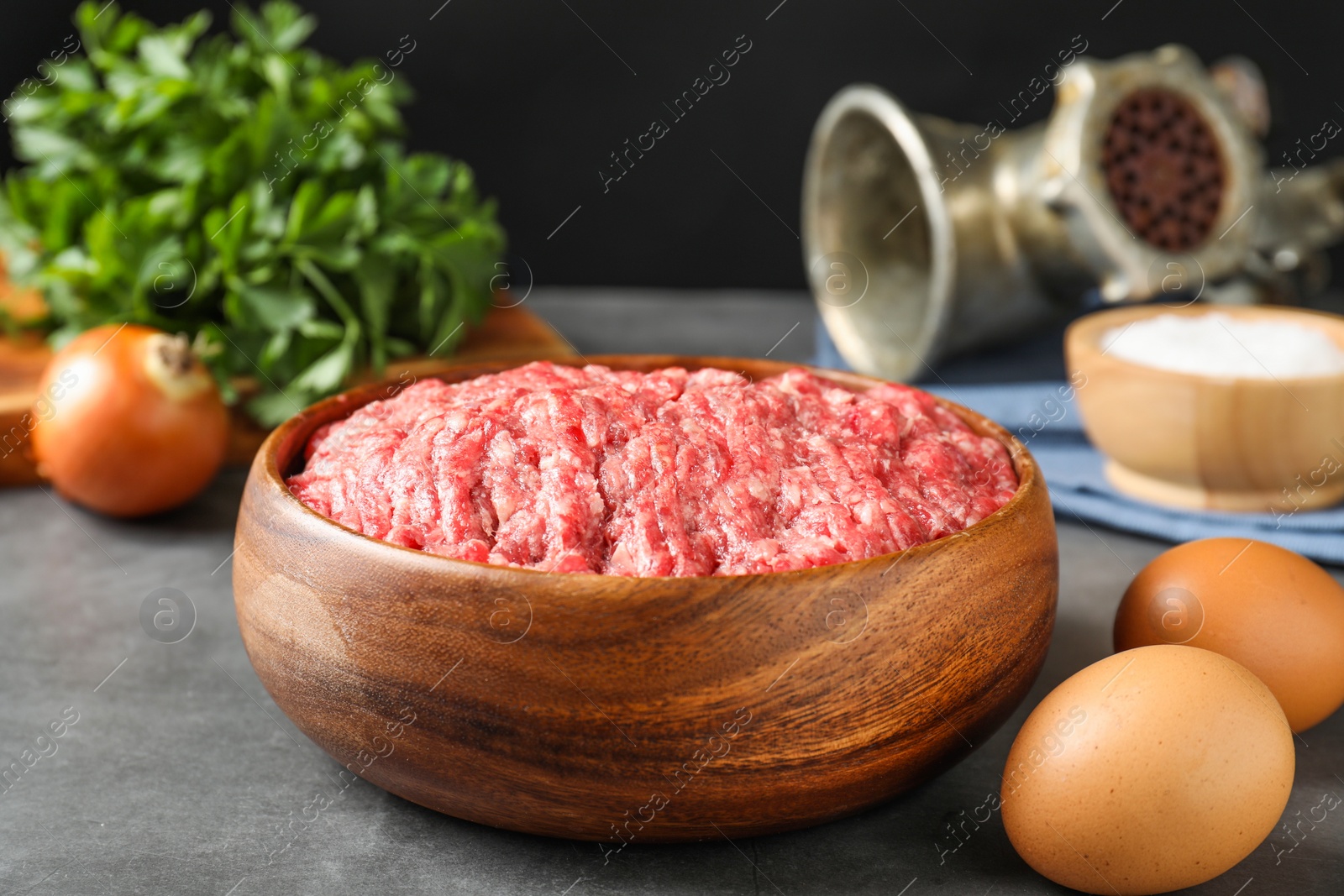 Photo of Raw ground meat in bowl and different products on grey table