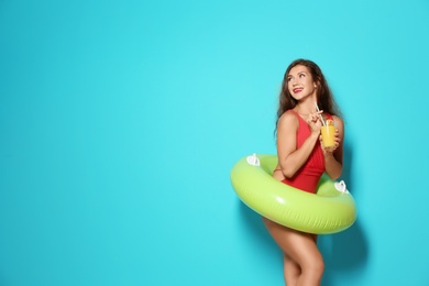 Beautiful young woman with inflatable ring and glass of cocktail on color background