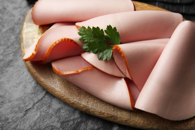 Board with slices of tasty boiled sausage and parsley on dark textured table, closeup