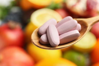 Photo of Vitamin pills in spoon against fresh fruits, closeup