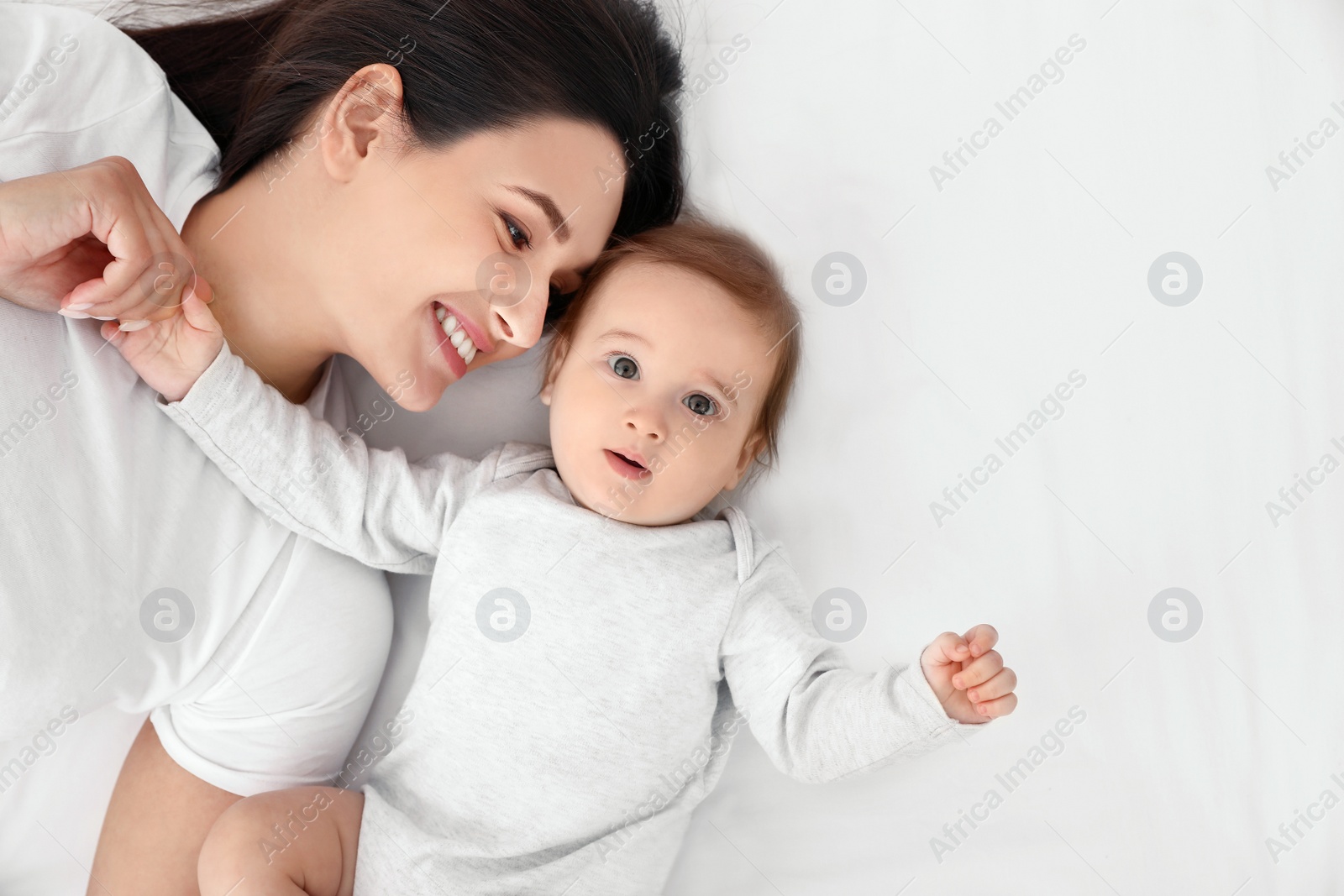 Photo of Portrait of mother with her cute baby lying on bed, top view. Space for text
