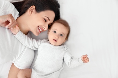 Photo of Portrait of mother with her cute baby lying on bed, top view. Space for text