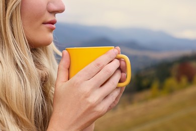 Photo of Young woman with mug of hot drink in mountains, closeup. Space for text