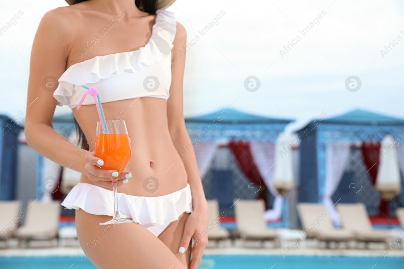 Photo of Young woman in stylish white bikini with cocktail near swimming pool, closeup. Space for text