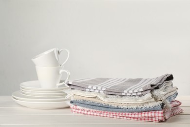 Stacked kitchen towels and dishware on white wooden table, space for text