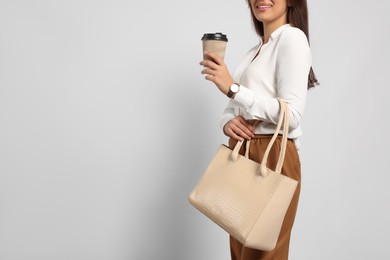 Young woman with stylish bag and cup of hot drink on white background, closeup