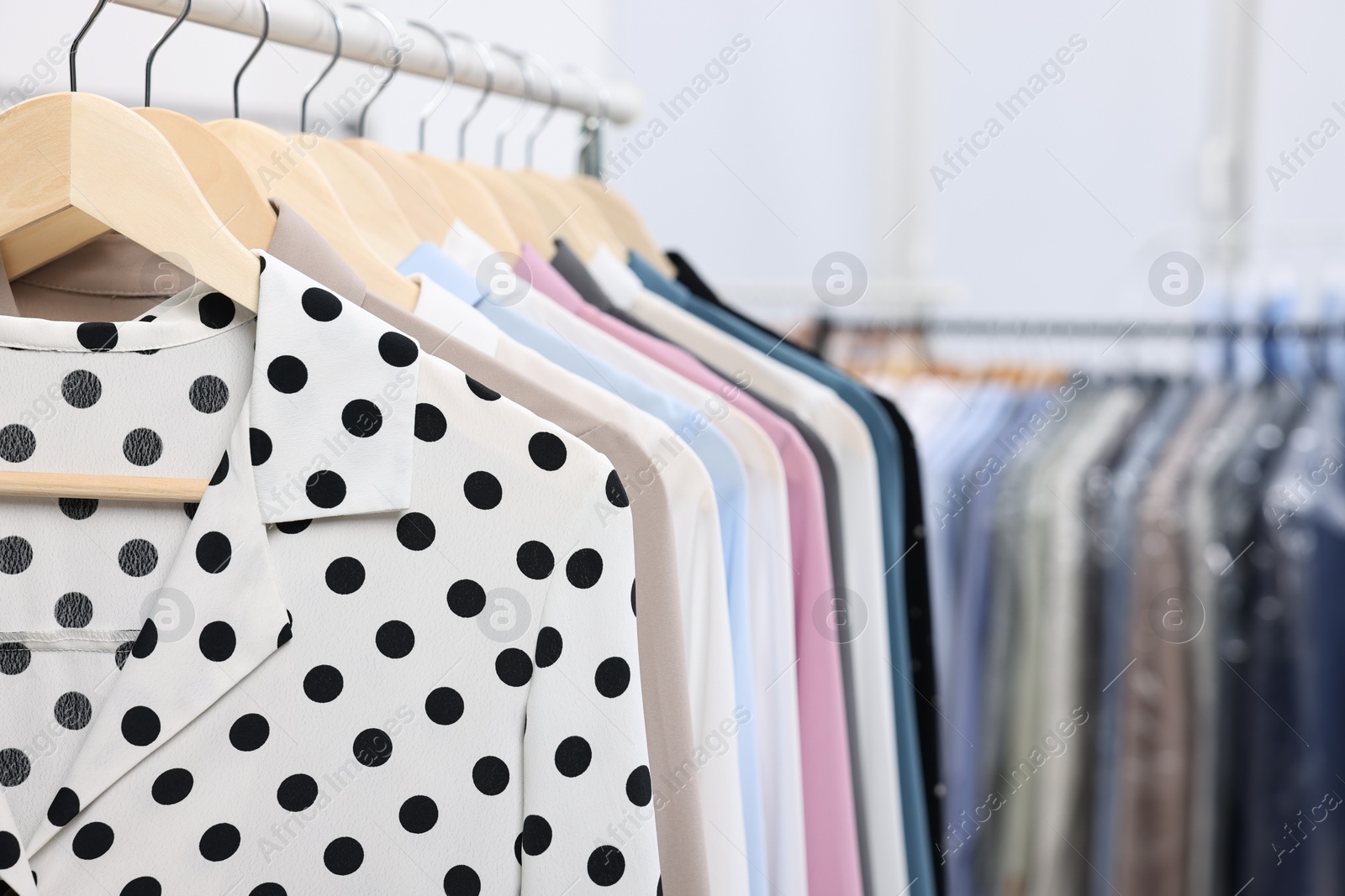 Photo of Dry-cleaning service. Many different clothes hanging on rack indoors, closeup