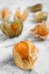 Ripe physalis fruits with dry husk on white marble table, closeup