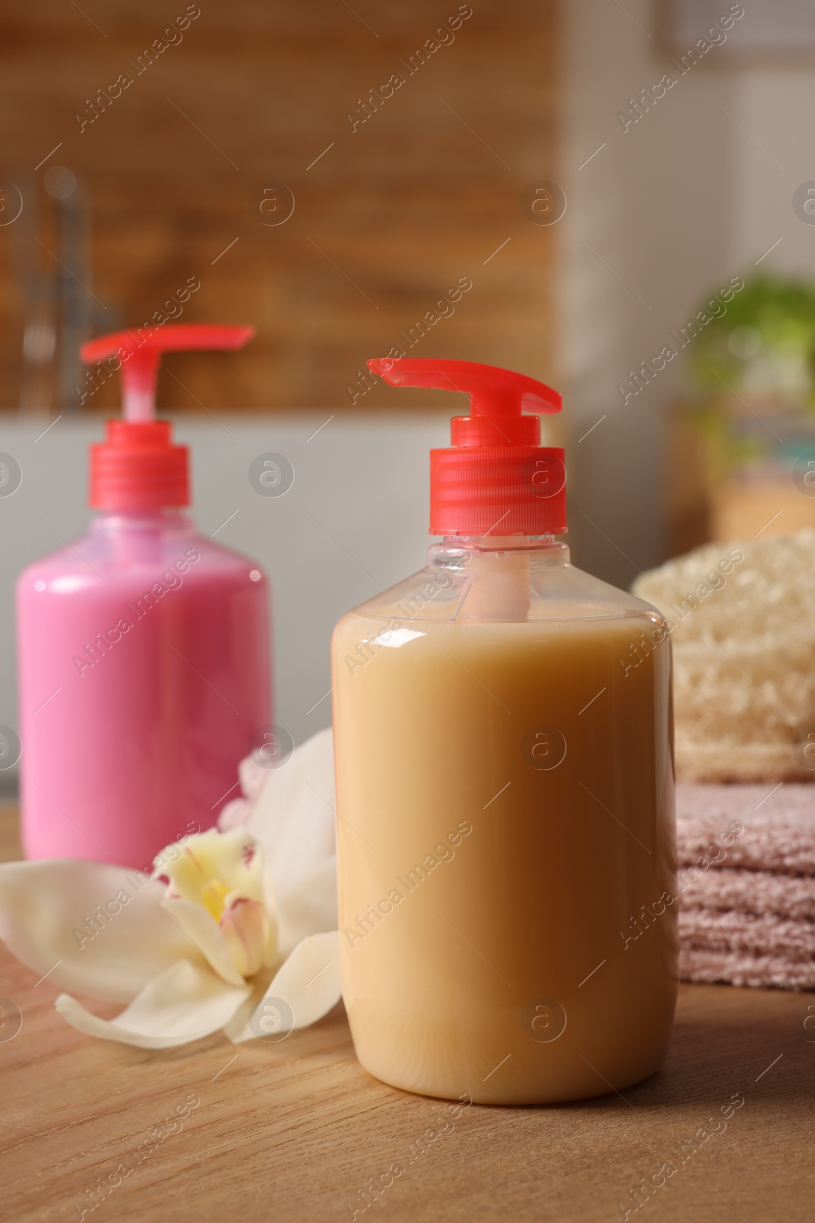 Photo of Dispensers of liquid soap and orchid flower on wooden table in bathroom