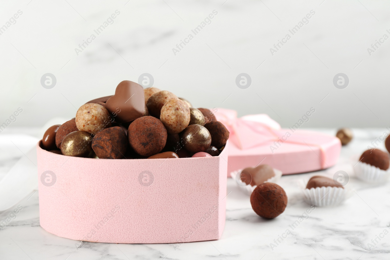 Photo of Different delicious chocolate candies in box on white marble table