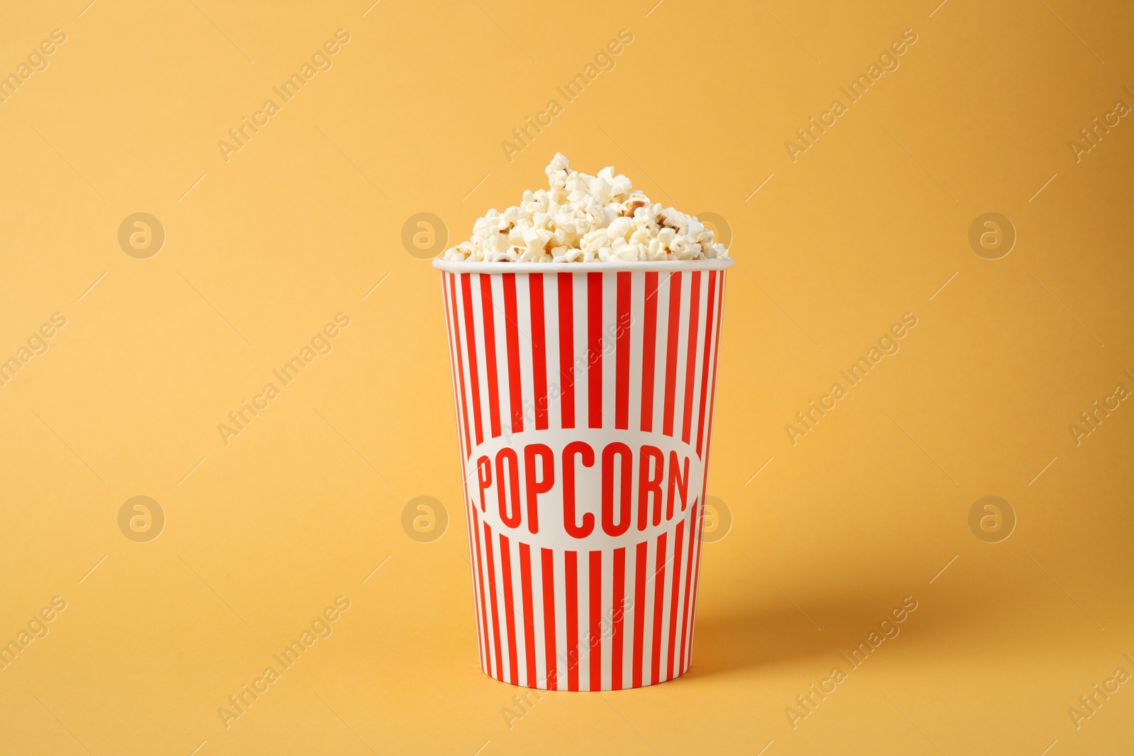 Photo of Delicious popcorn in paper cup on yellow background