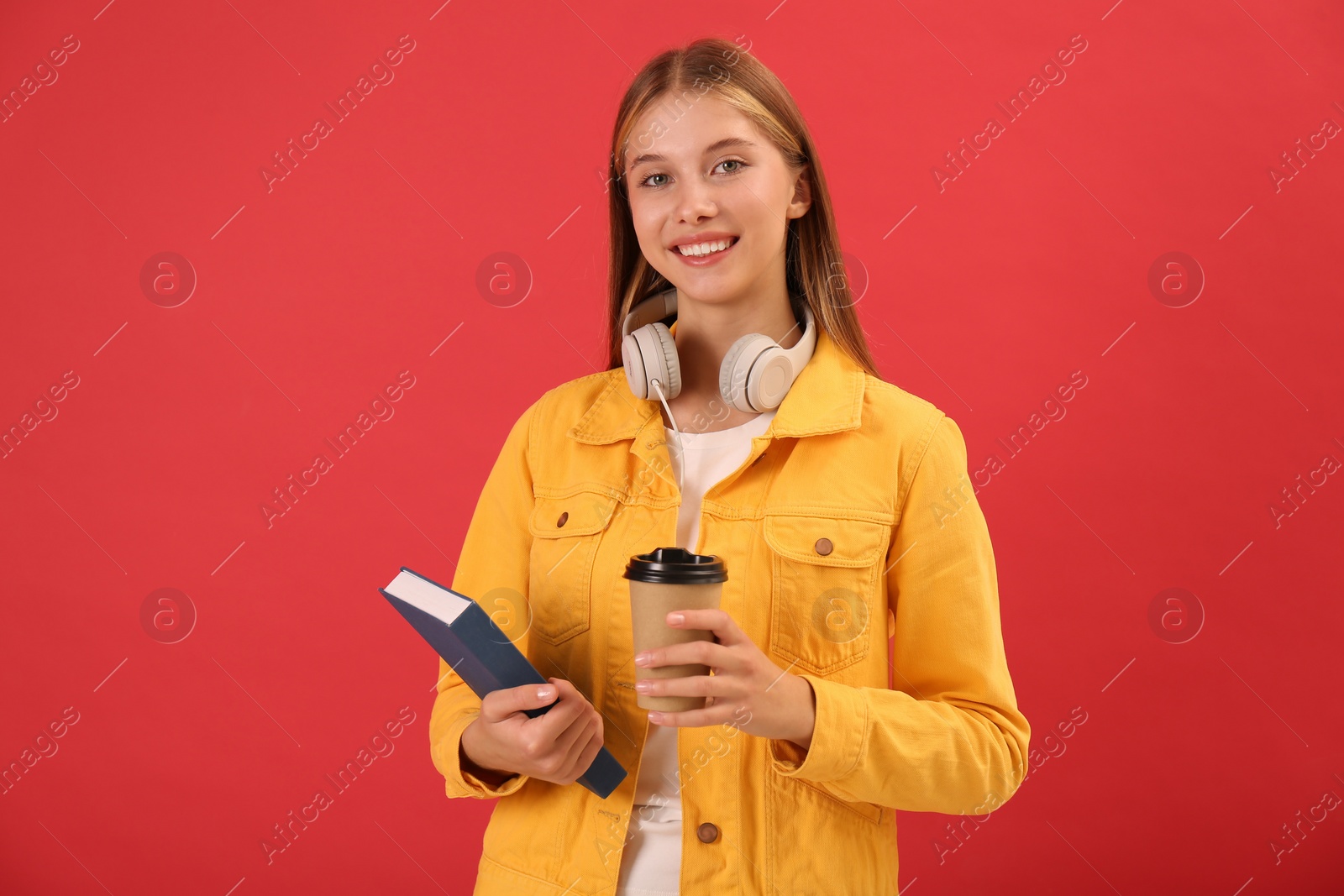 Photo of Teenage student with book, cup of coffee and headphones on red background