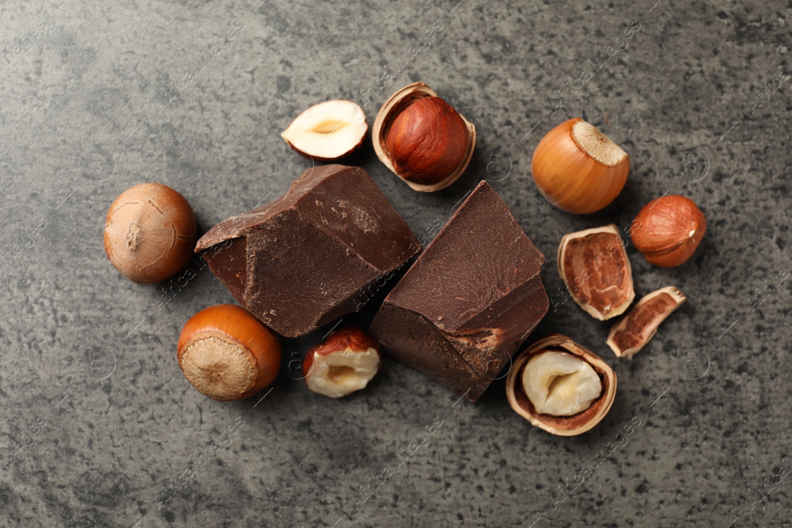 Photo of Delicious chocolate chunks and hazelnuts on grey table, flat lay