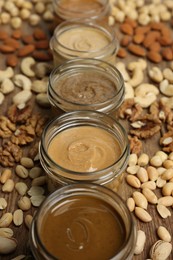 Nut butters in bowls and ingredients on wooden table, closeup